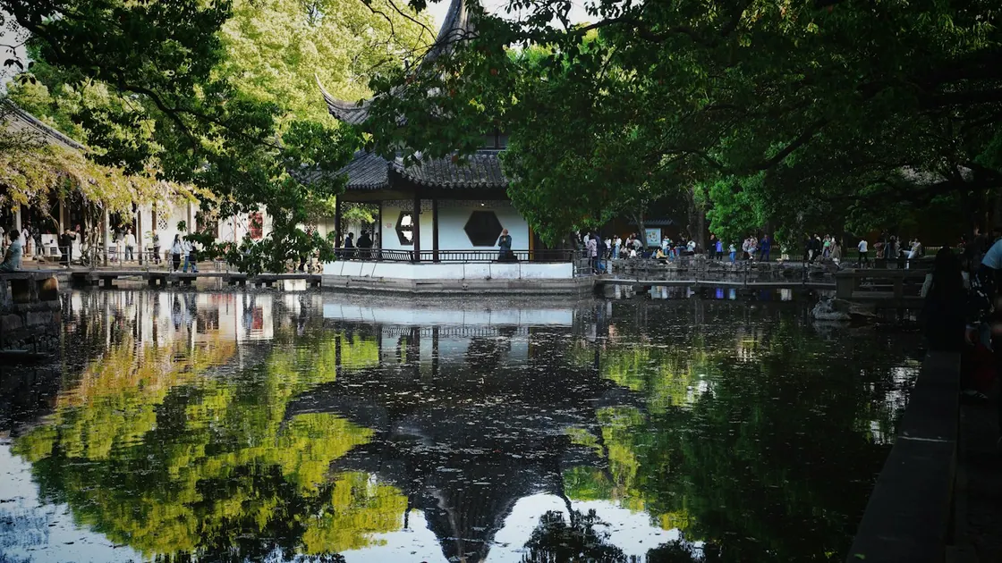 A classical garden pavilion and its reflection in a still pond, framed by trees