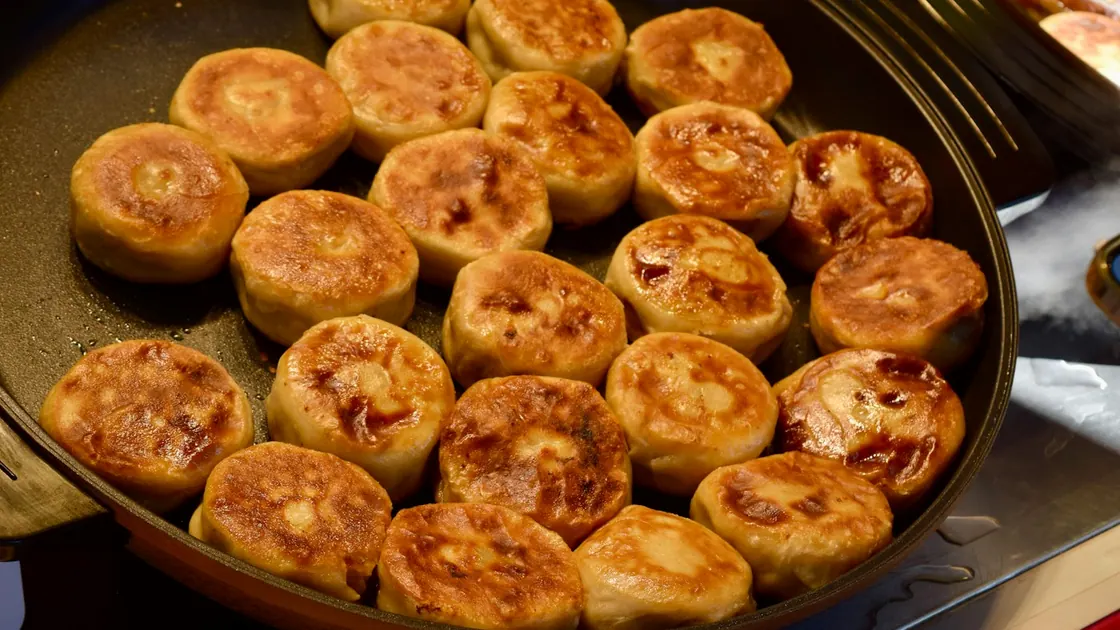 Rows of pan-fried buns browning in a large black pan