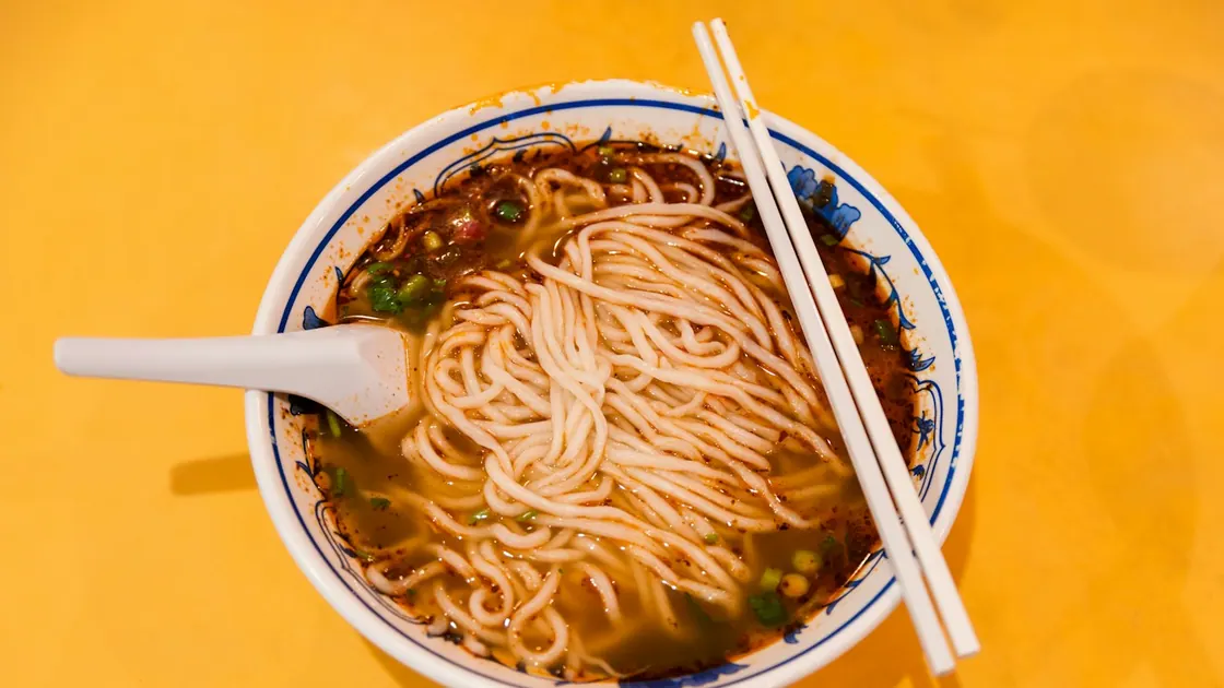 A bowl of thin noodles in broth with chopsticks and a spoon