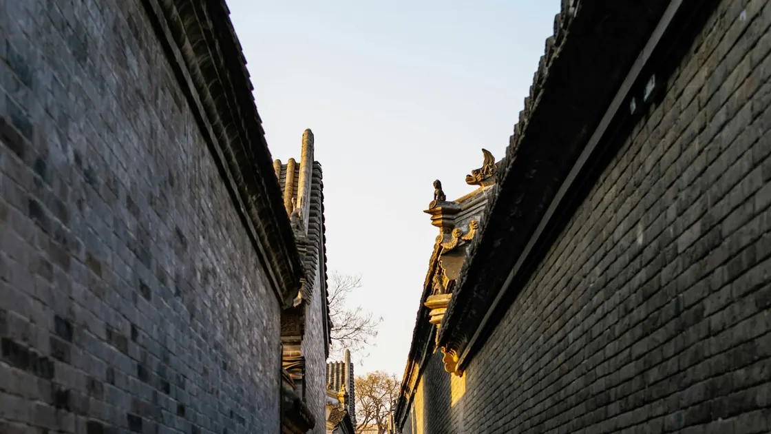 Looking up between two high grey brick walls of a Chinese city wall, with glazed roof ornaments catching the light