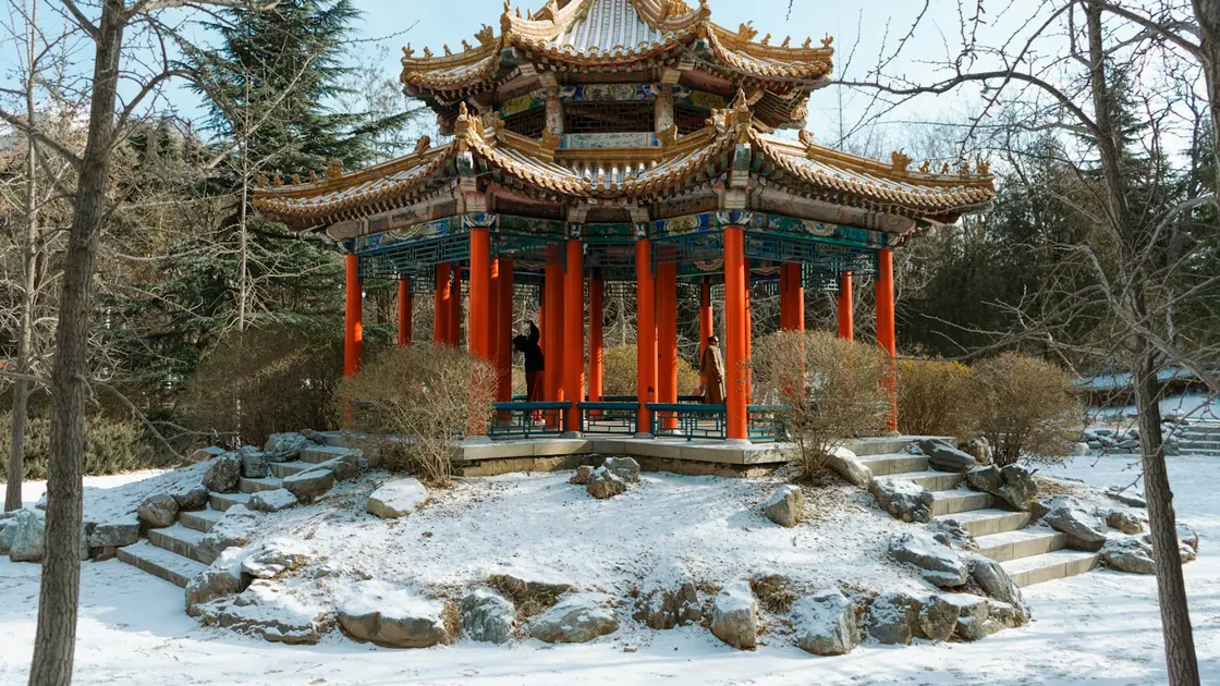 A snow-covered Chinese pavilion with red columns and painted beams